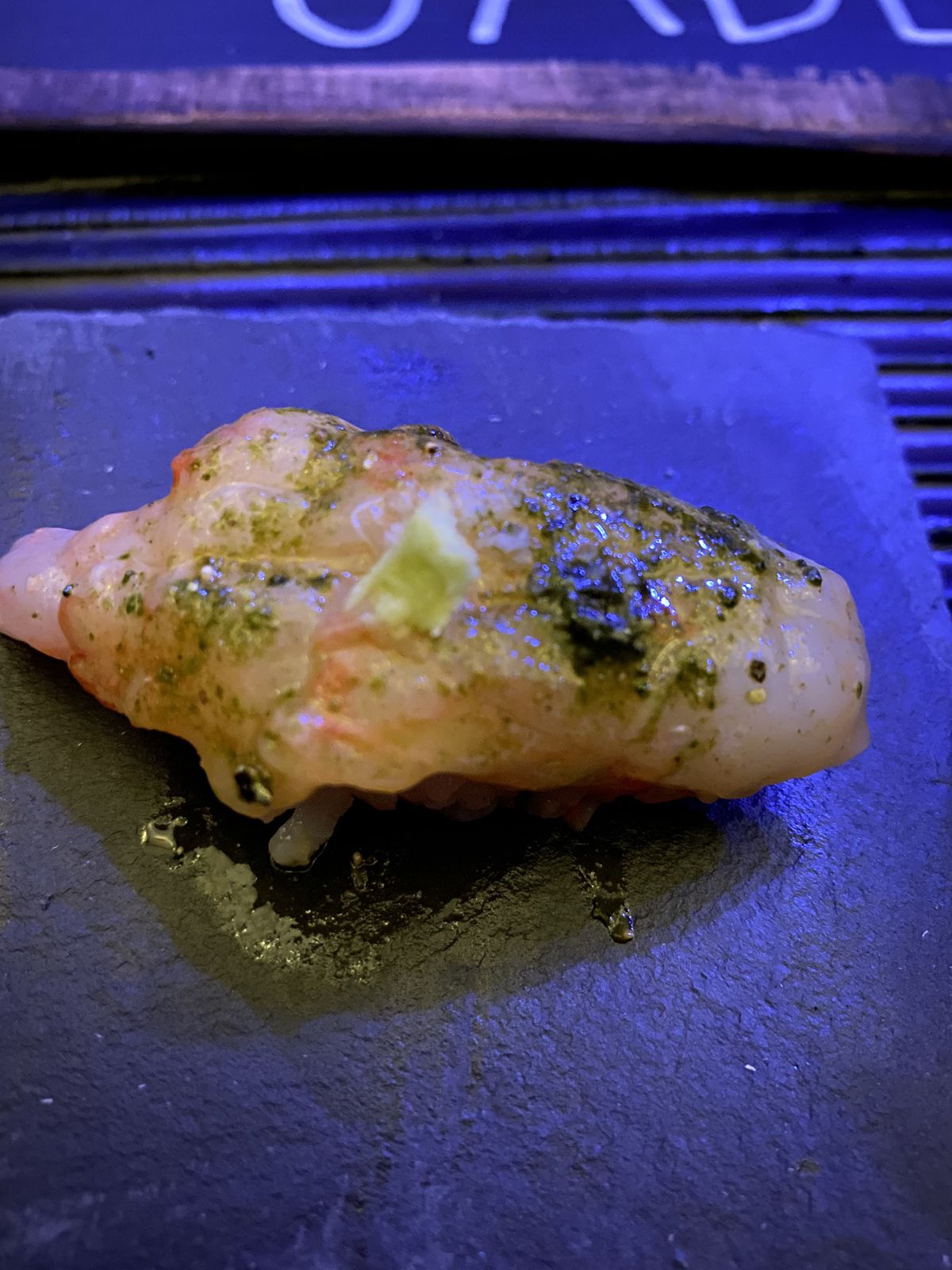 A piece of raw spot prawn nigiri, glistening with oil and garnished with wasabi. 