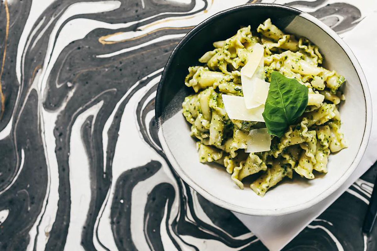 A bowl of pesto-topped pasta sits atop a black and white swirled table top