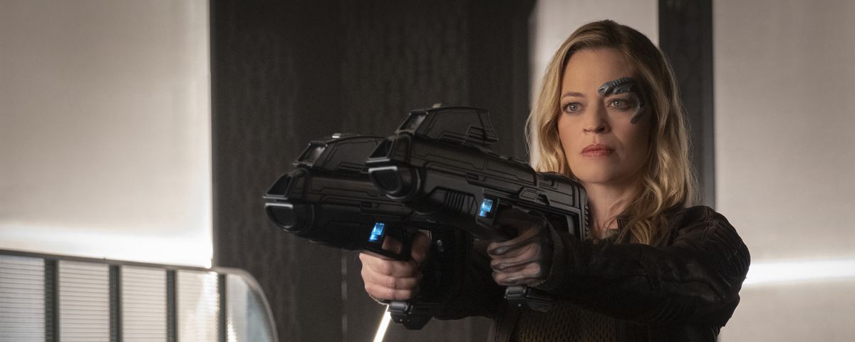 A determined-looking blonde woman with Borg face implants —&nbsp;Seven of Nine from Star Trek: Voyager, played by Jeri Ryan — points two phaser rifles at a target offscreen.