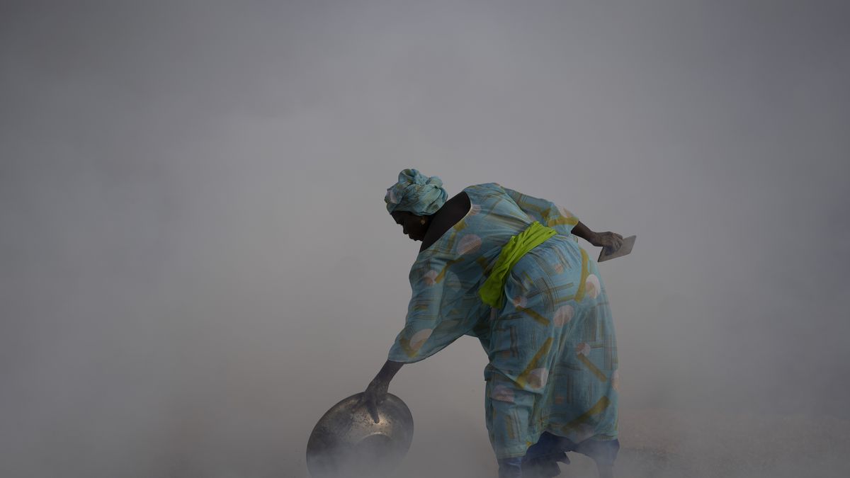 Ndeye Yacine Dieng drops embers over peanut shells covering fish as she walks amidst the smoke on Bargny beach, some 22 miles east of Dakar, Senegal, Wednesday April 21, 2021. 