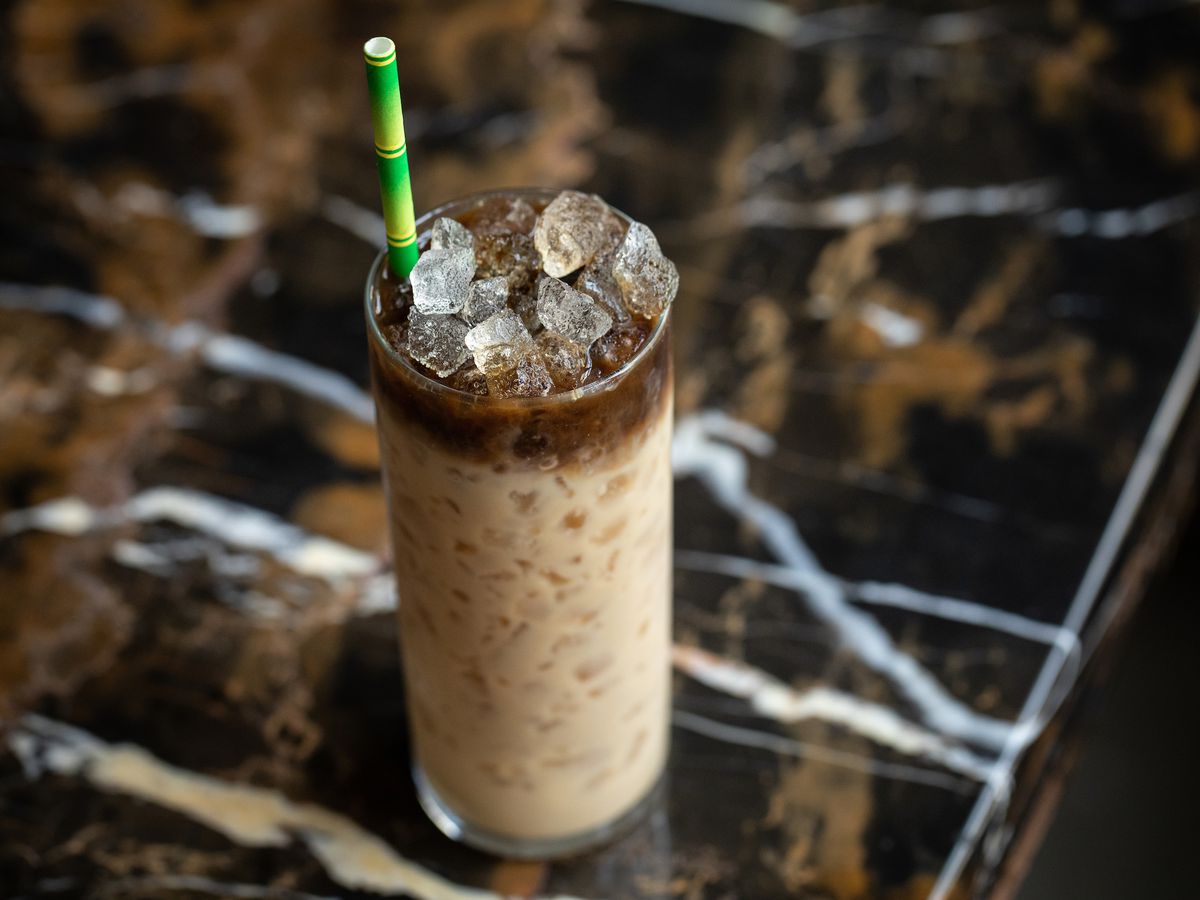 A coffee cocktail in a long cylindrical glass with a green and white paper straw poking out between ice cubes