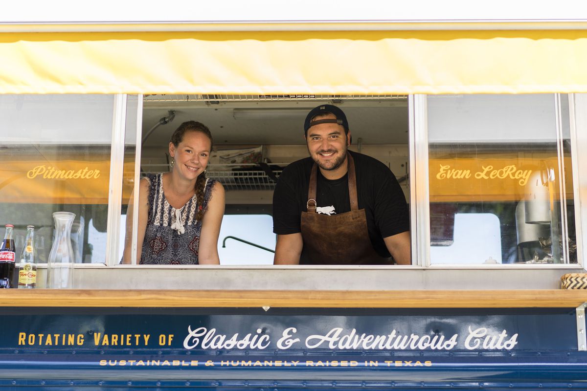 A man and a woman in aprons in a food truck window. 