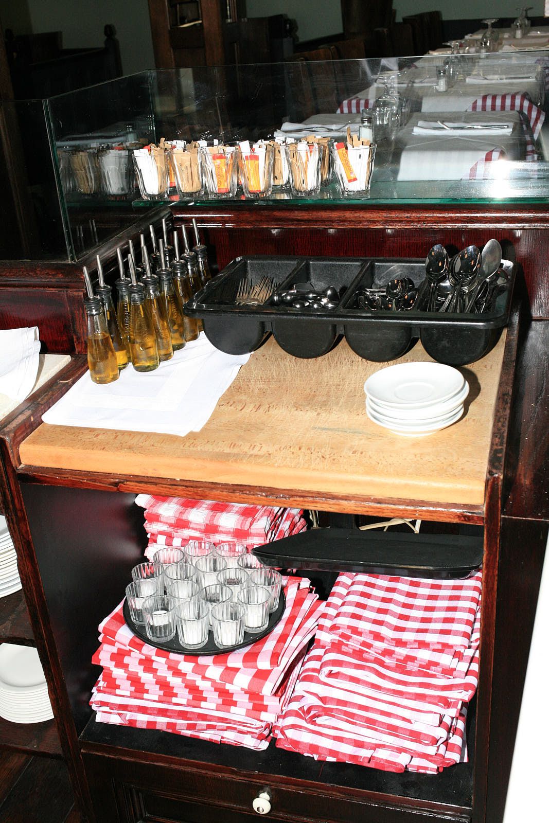 A bar cart stocked with cutlery, tablecloths, napkins, and gingham drapes.