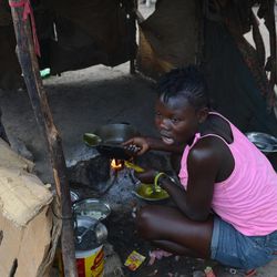 In this March 21, 2015 photo, a teenage girl is cooks the family's evening meal inside a makeshift tent of flattened cardboard boxes and cloth at a borderland encampment outside the southeast Haitian town of Anse-a-Pitres, Haiti. The encampment is filled with people who either fled or were deported from the neighboring Dominican Republic amid an immigration crackdown. Within a month, authorities hope to move nearly 2,400 people in a half-dozen encampments by providing enough money for them to rent homes for a year in nearby towns. 