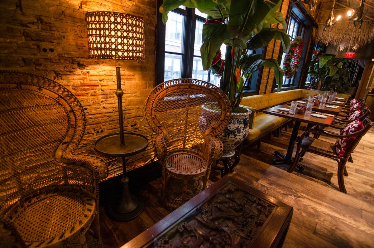 Two wooden peacock-style chairs sit in front of an intricately carved wooden table in a tiki-themed restaurant.