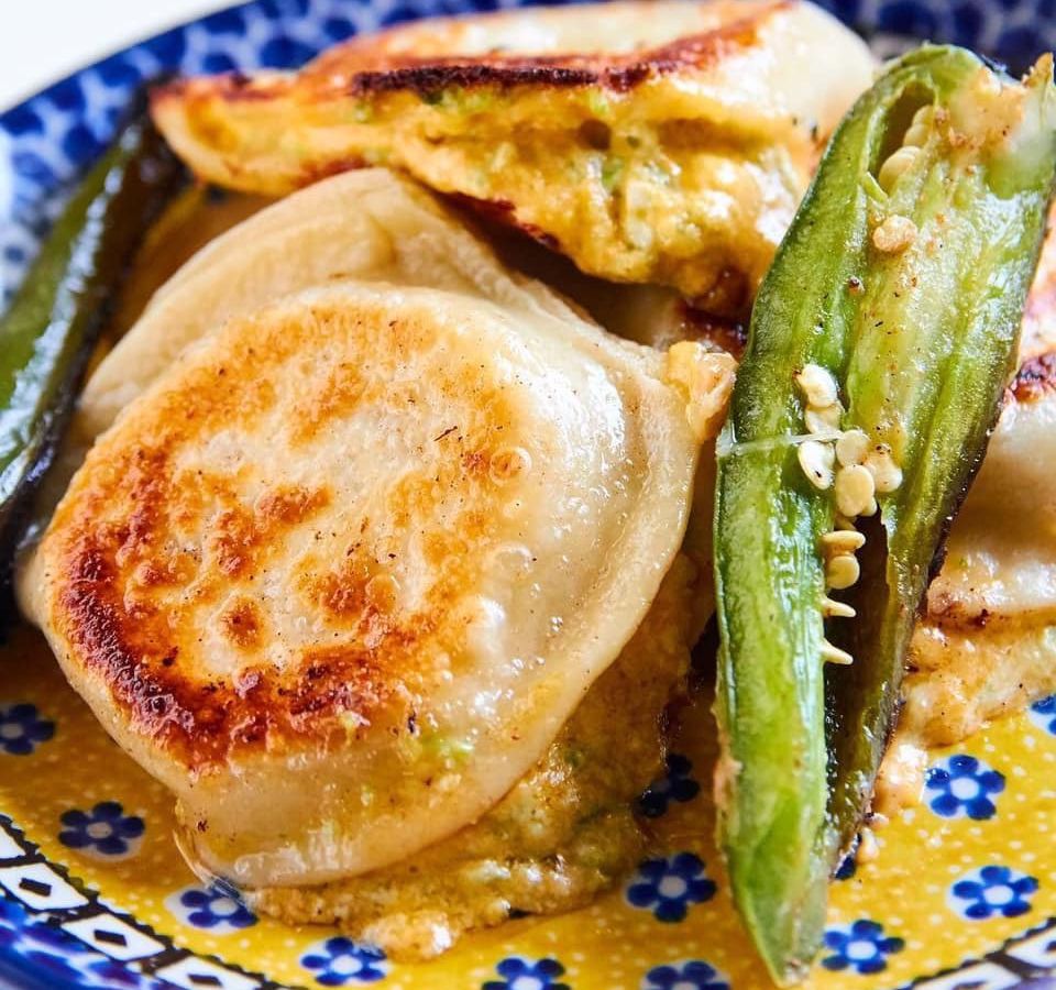 A pile of pan fried pierogi with a fried jalapeno sliced in half on a decorative canary blue and yellow Polish plate.