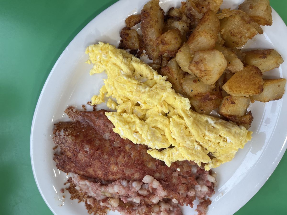 A plate of scrambled eggs, corned beef hash, and potatoes.