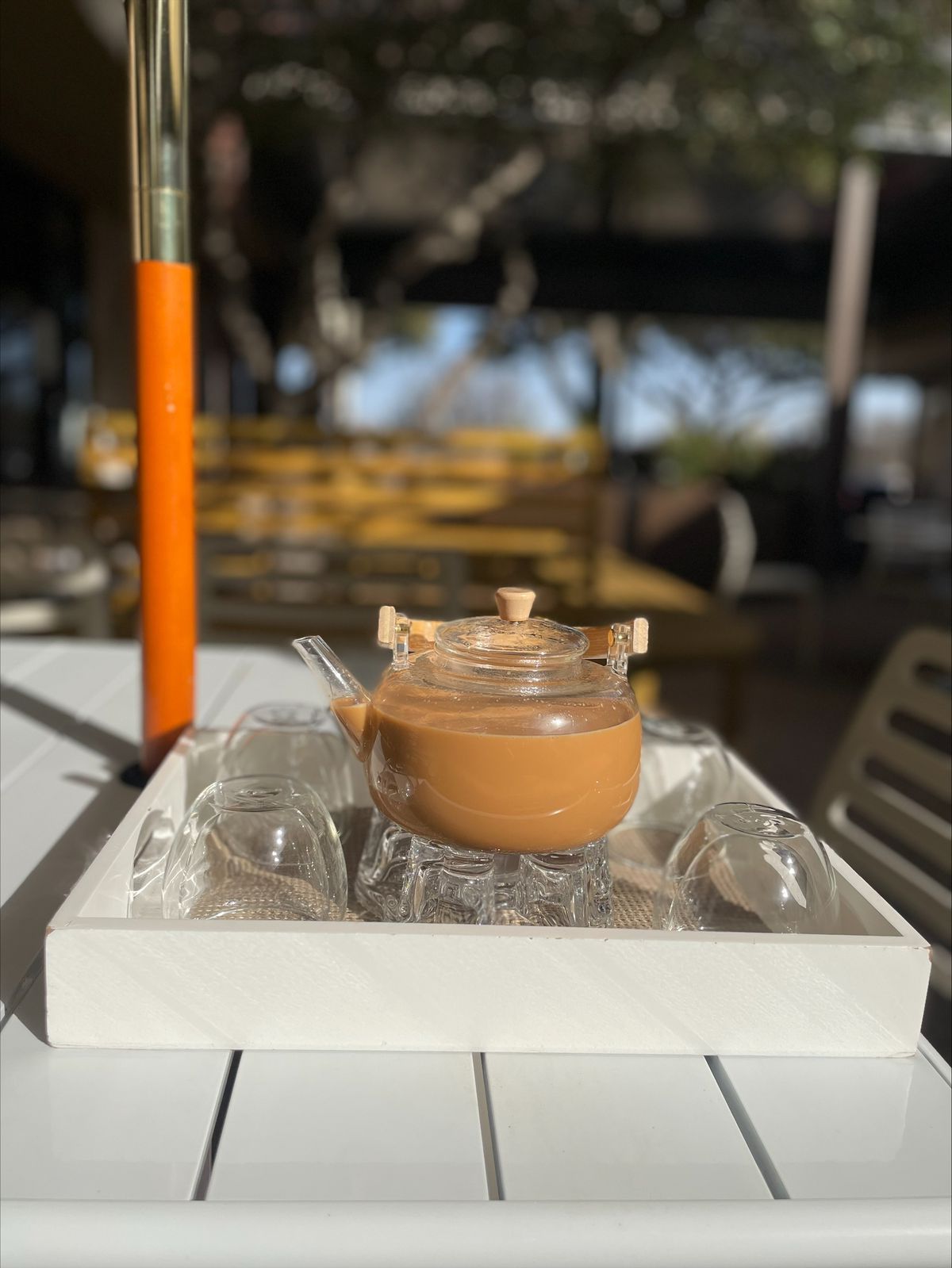 A glass coffee pot with light brown liquid sits on a tray on an outdoor table.