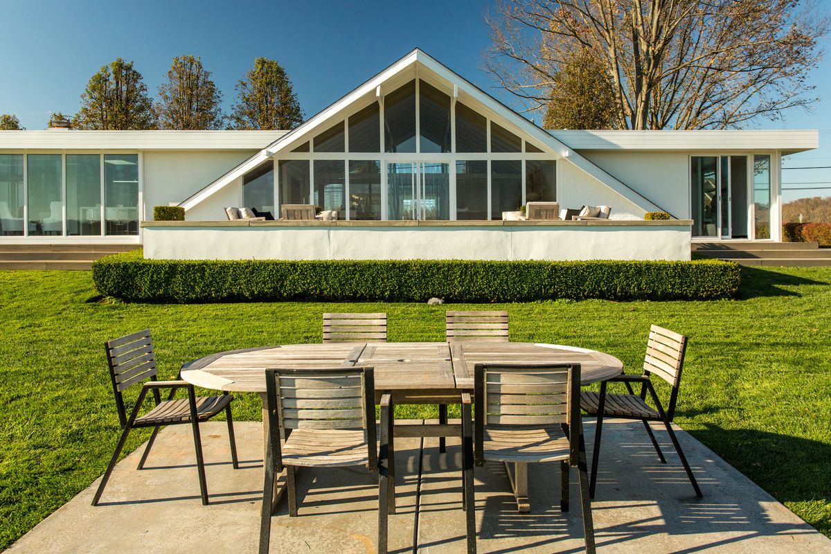 An exterior view of the house shows an outdoor dining set in the foreground, and the A-frame house in the background.