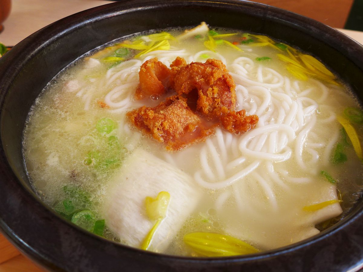 A black bowl of rice noodles in broth with several additional ingredients.