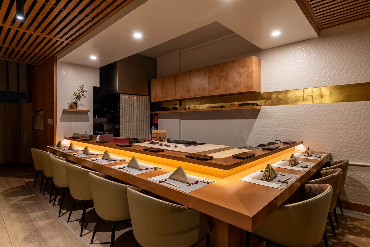 Dimly lit, minimalist sushi bar with ornate gold wall design and white textured tiles.