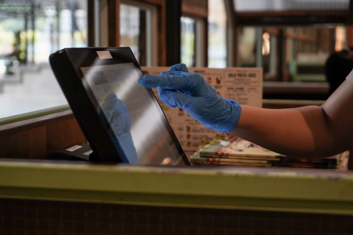 An employee using a cash register while wearing gloves