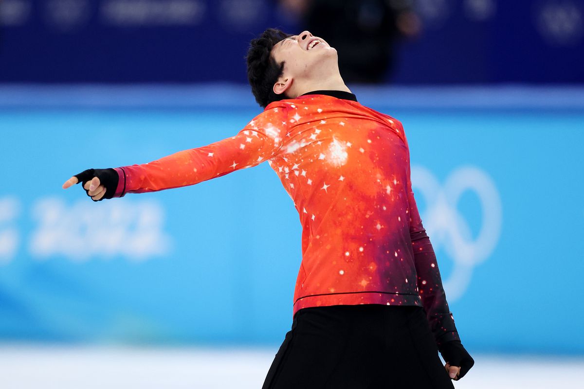 Figure skater Nathan Chen standing on the ice with one arm outstretched and his head thrown back.