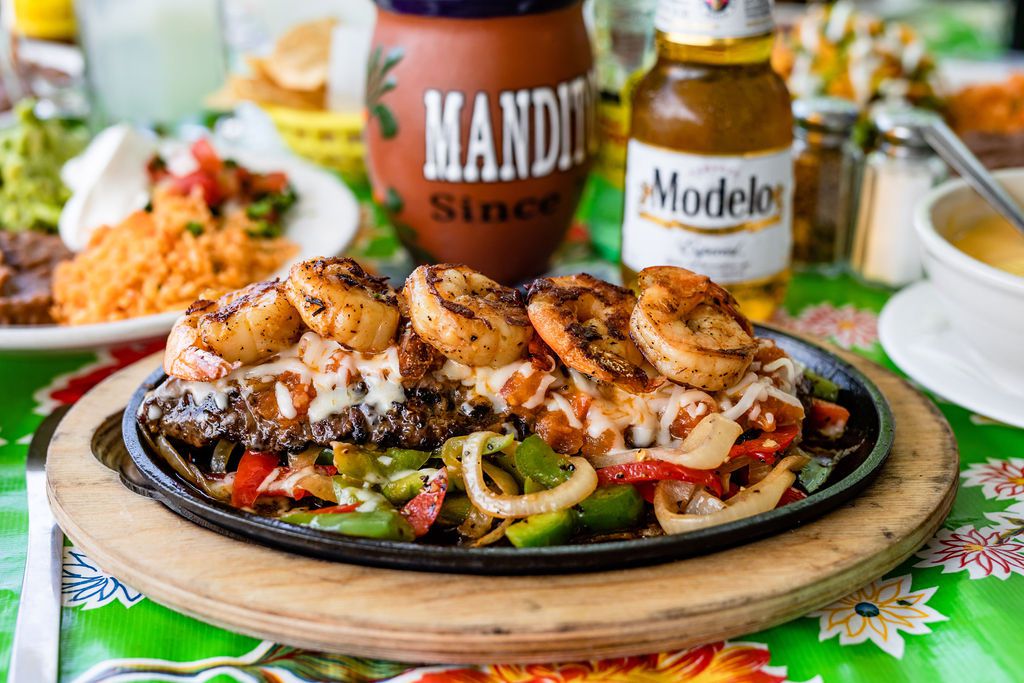 Mandito’s carne asada fajitas topped with bell peppers and shrimp, served with a Modelo.