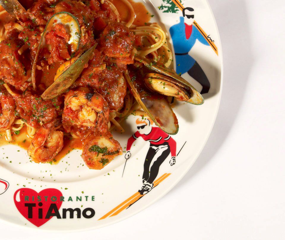 A plate illustrated with simple skier figures filled with mussels, shrimp, and scallops in sauce over linguine