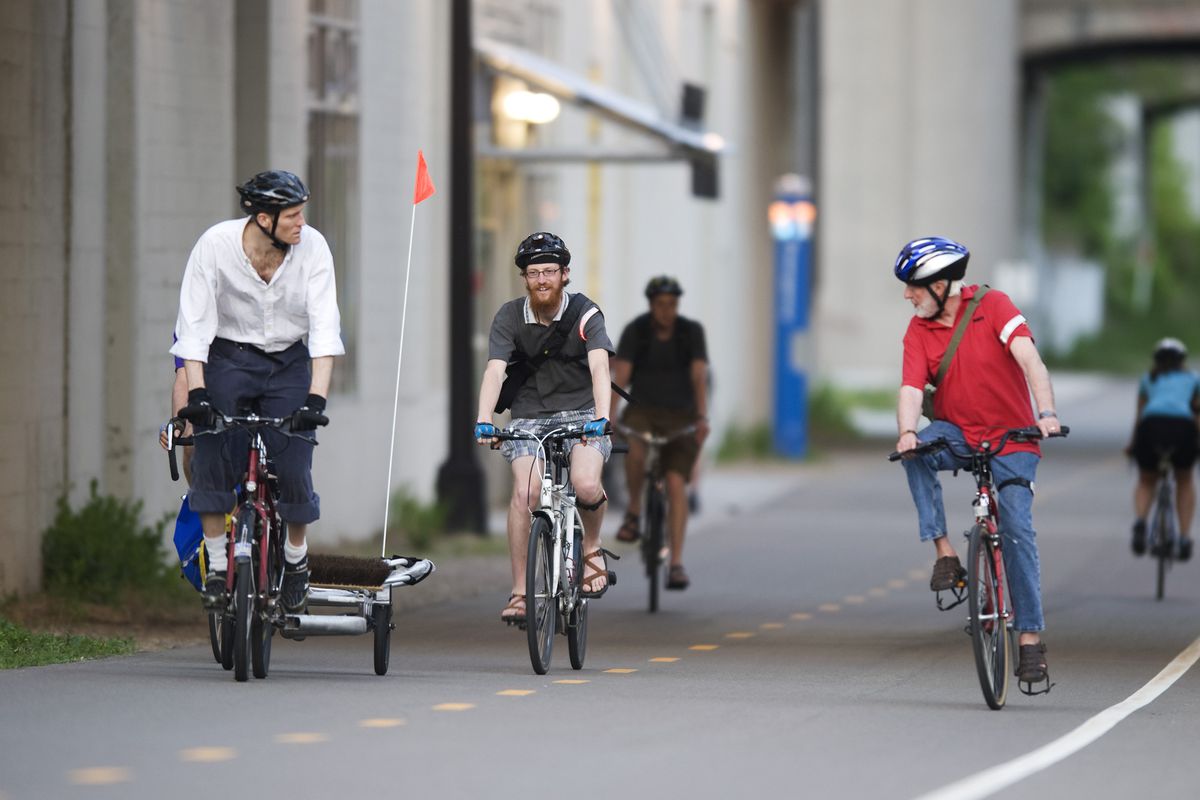 Five cyclists in casual clothing are seen along a wide, divided bike path
