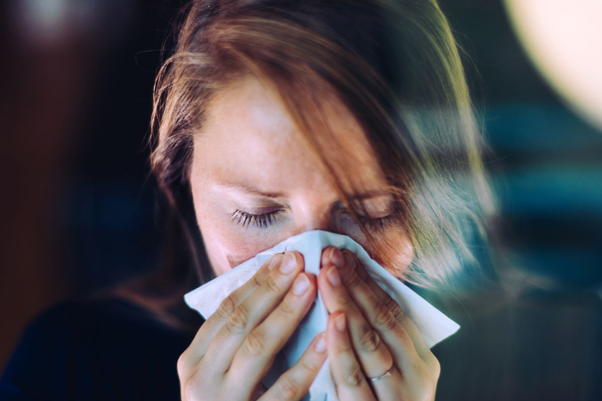 A woman holds a tissue to her nose as she sneezes.