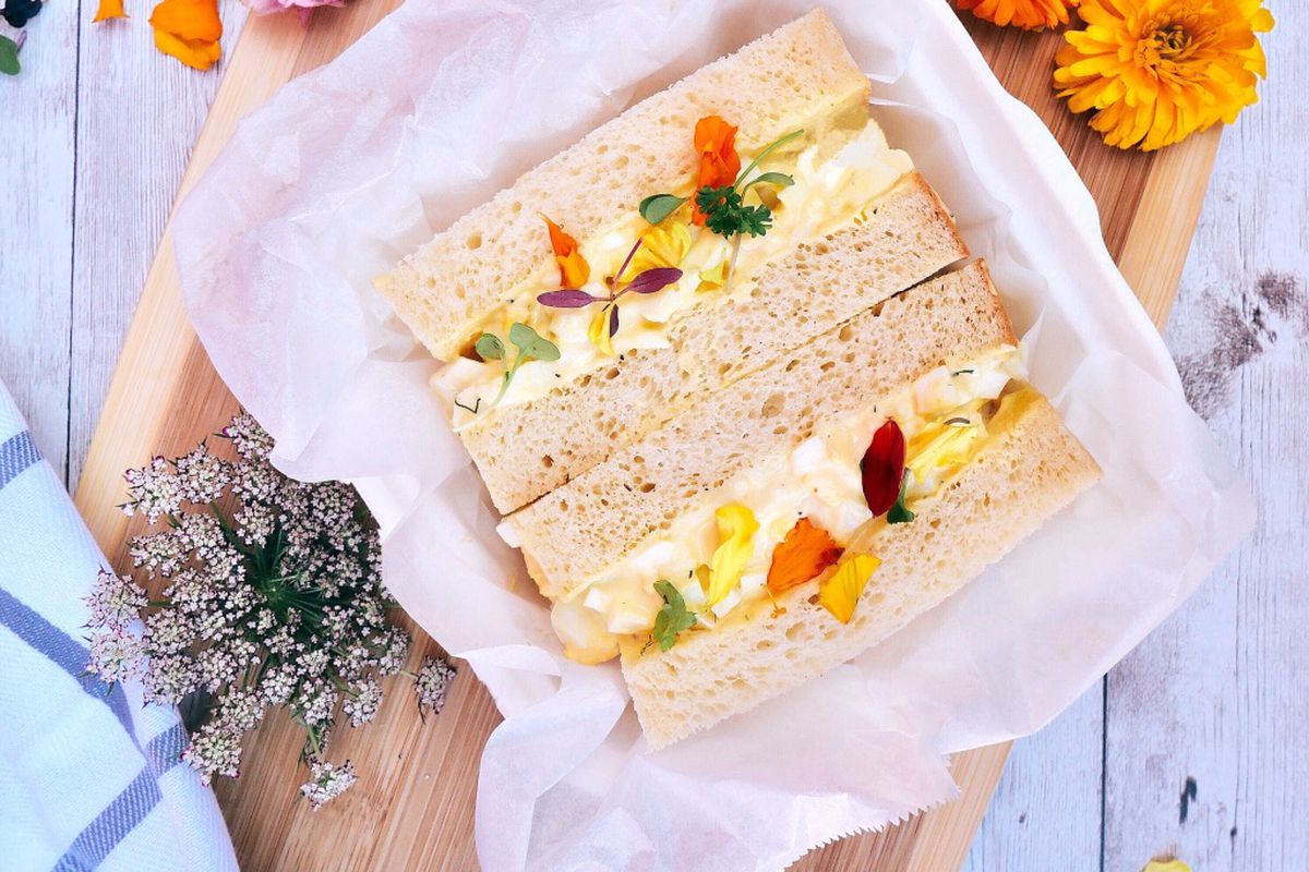 An egg salad sandwich with the crusts cut off and edible flowers at the new Bread n’ Chu