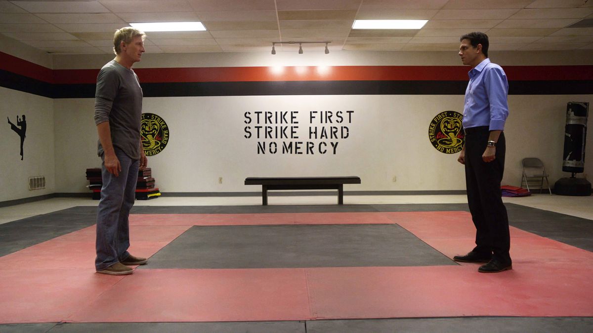 Johnny Lawrence (left) and Daniel LaRusso (right) face each other in present day in the Cobra Kai dojo, whose motto is still “Strike First, Strike Hard, No Mercy.”