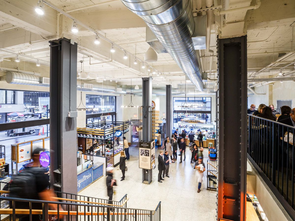 The spacious interior of Urbanspace at 570 Lex, showing people sitting and standing on both of the food hall’s two-story levels.