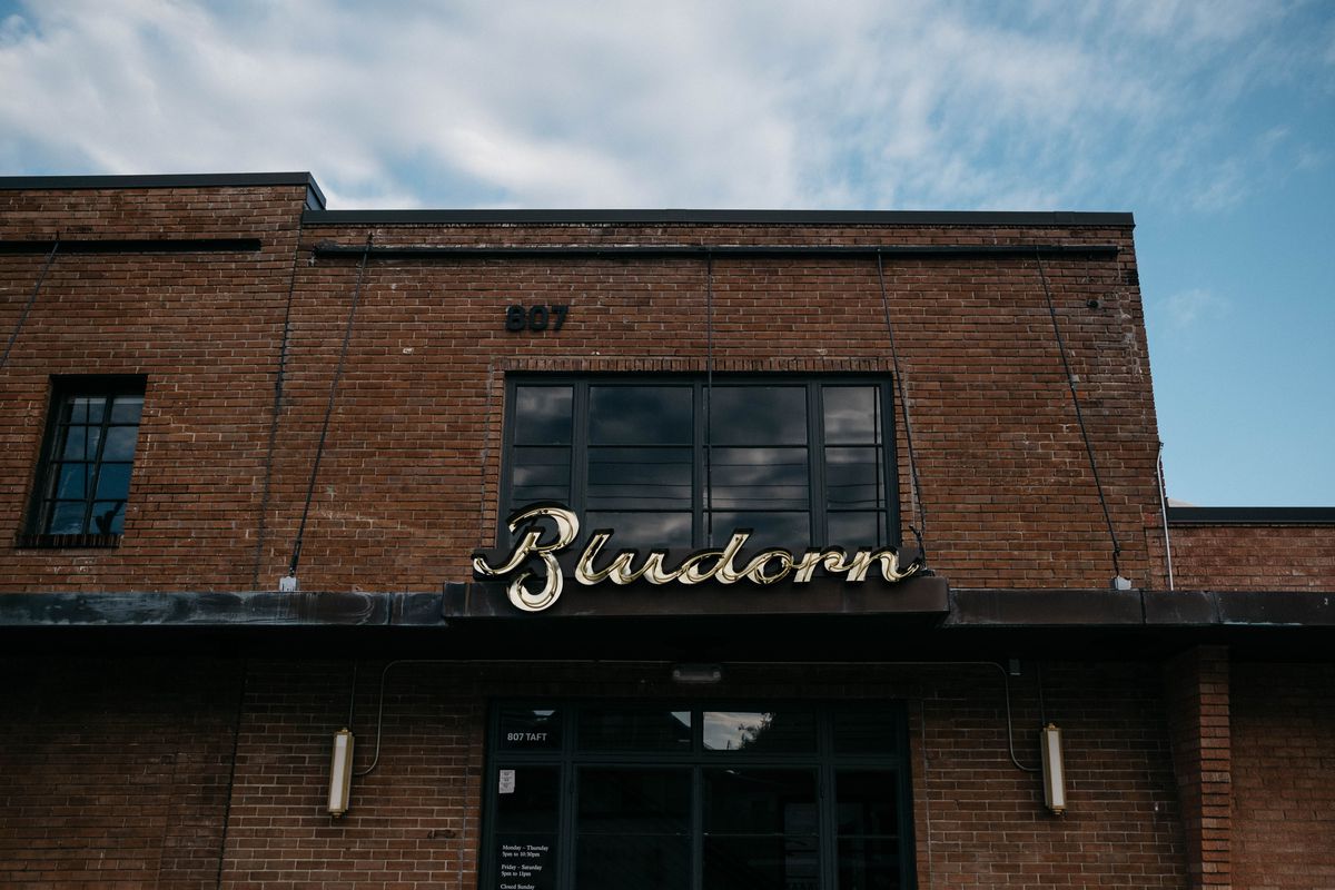 A large, square brick building with tall windows and an overhang with a vintage-looking sign reading “Bludorn.”
