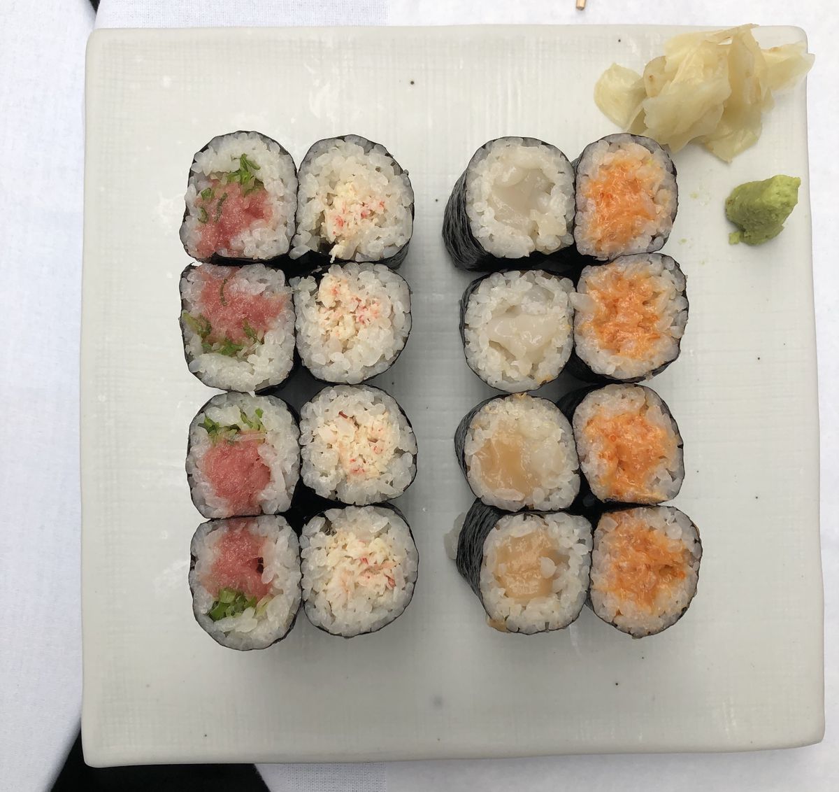 A rectangular white plate with rows of sushi placed on top of it