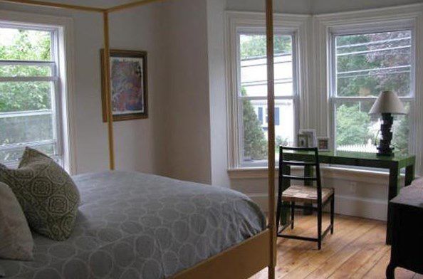 A bedroom with a bed facing a desk and chair in front of a bay window. 
