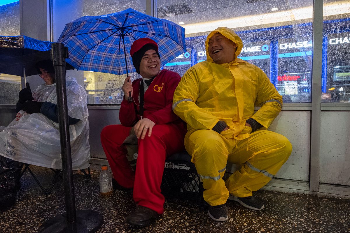 Paulo Bautista (left, 26) shares a makeshift plastic basket seat with Marvin Briones (right, 34) as they wait in the pouring rain for the opening of Jollibee.