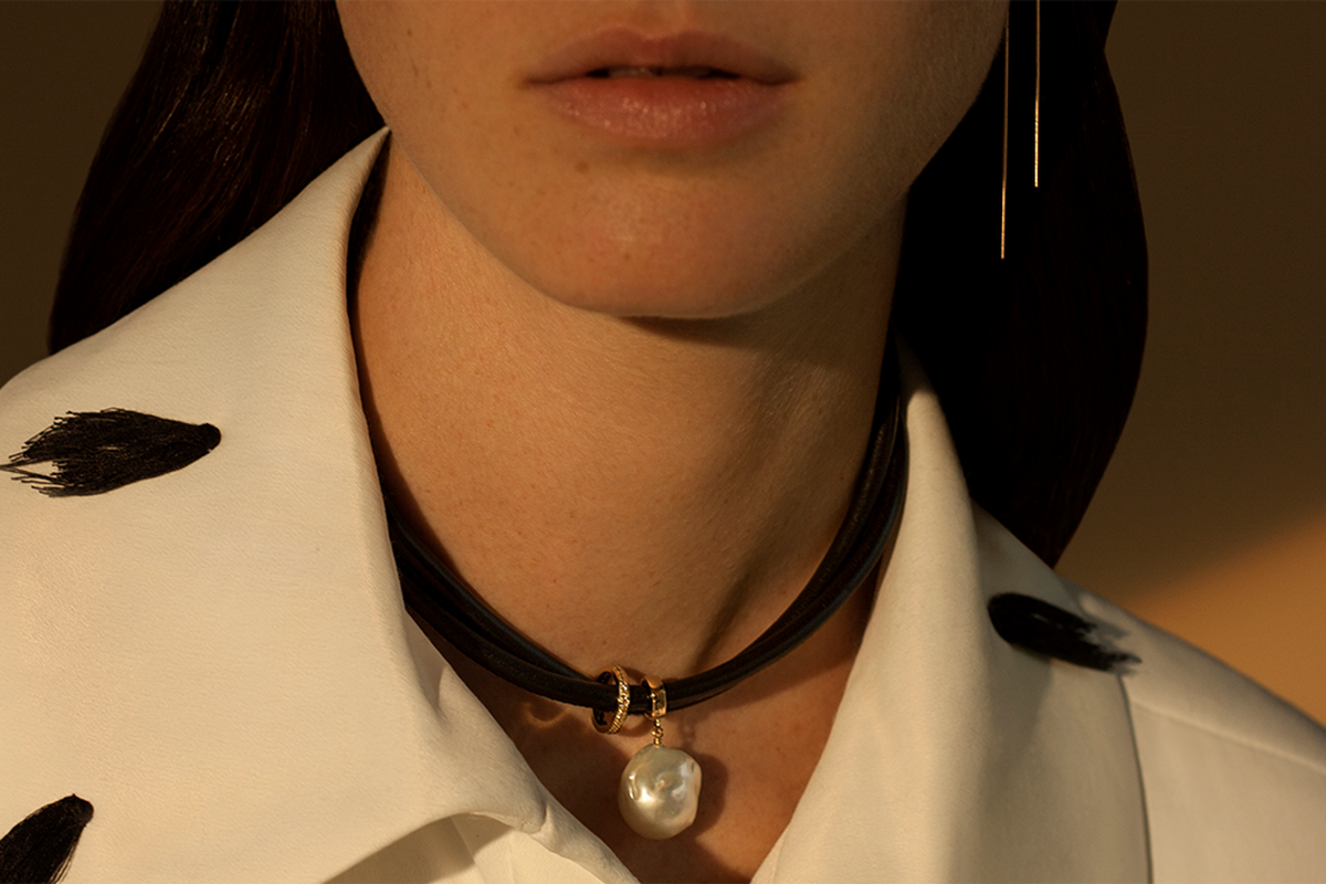 A close up of a woman wearing a choker with a center pearl.