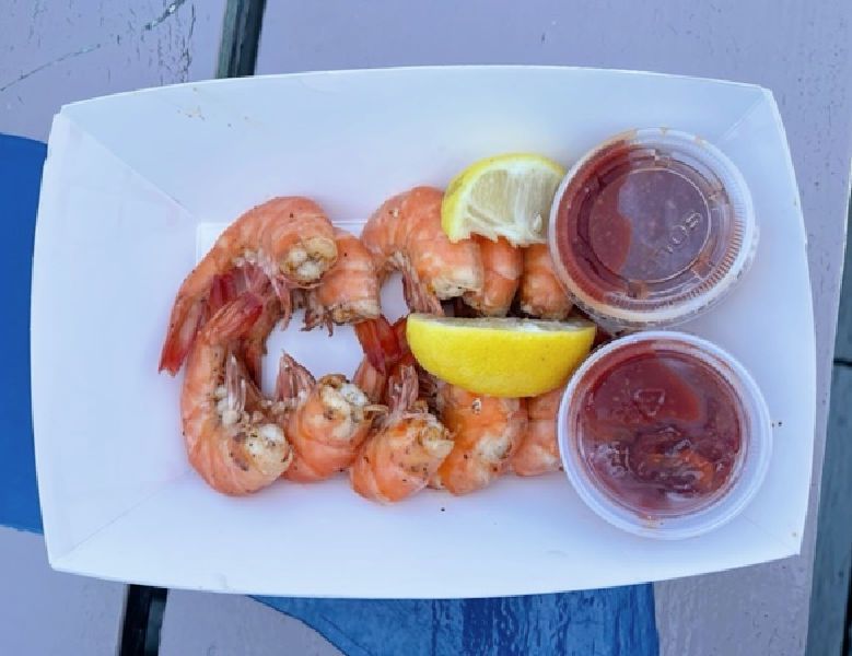 A dozen peel-and-eat shrimp with cocktail sauce in a paper boat.