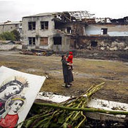A woman carrying a child walks in the yard of the ruined school in Beslan, Russia, where the violent hostage crisis took place.