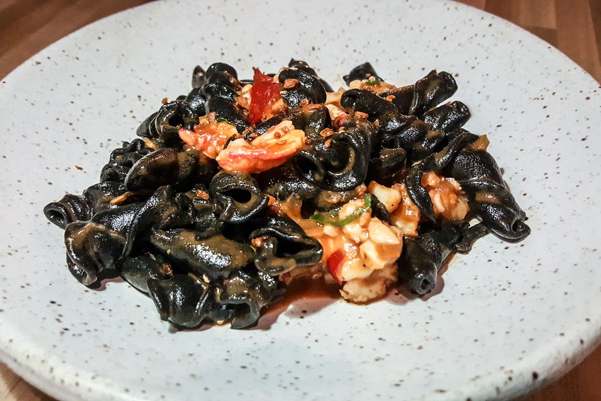 Black campanelle pasta with chunks of lobster on an earthy, white-speckled plate
