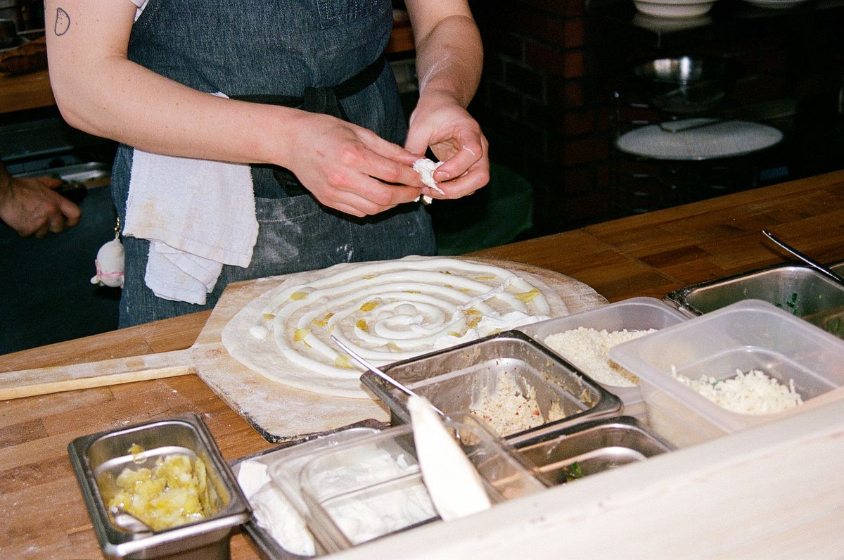 A chef places pieces of cheese on uncooked pizza dough at Cafe Olli.