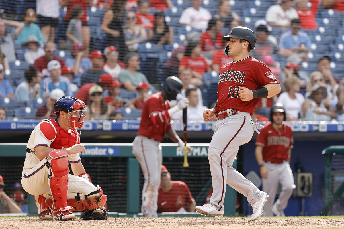 Dalton Varsho steps on home while scoring a run. The Phillies’ catcher looks on in disgust, while a very disinterested crowd can be seen in the background