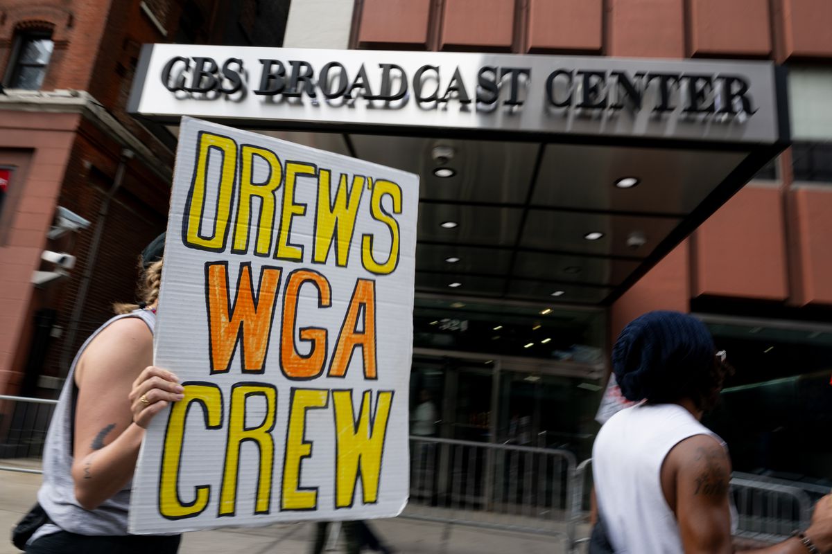 A picketer holds a sign that says “Drews WGA Crew” in front of CBS studios.