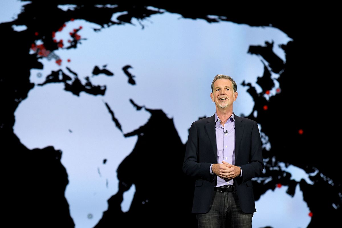 Reed Hastings, CEO of Netflix International stands before a map of the world as he speaks on a stage. 