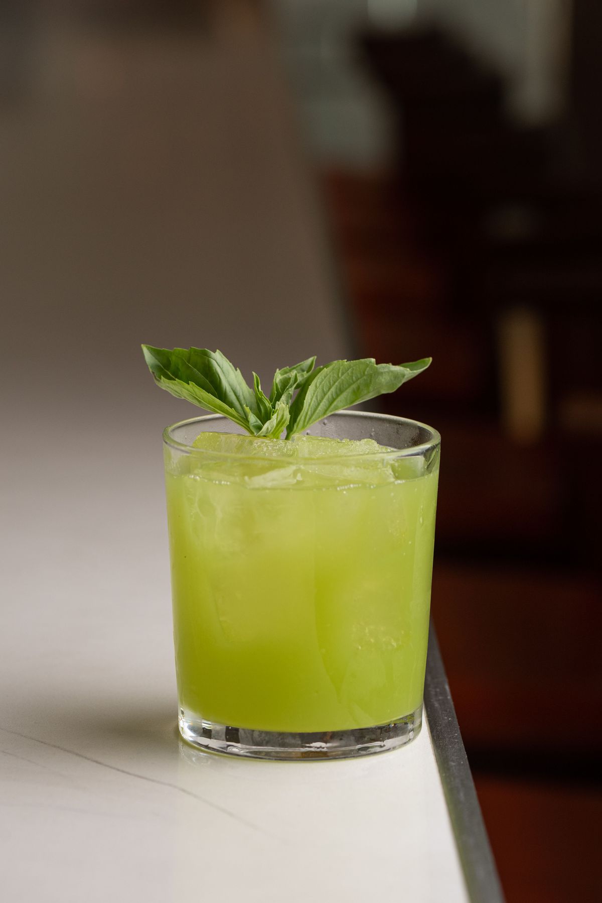A light. green cocktail in a wide glass on the edge of a marble table.