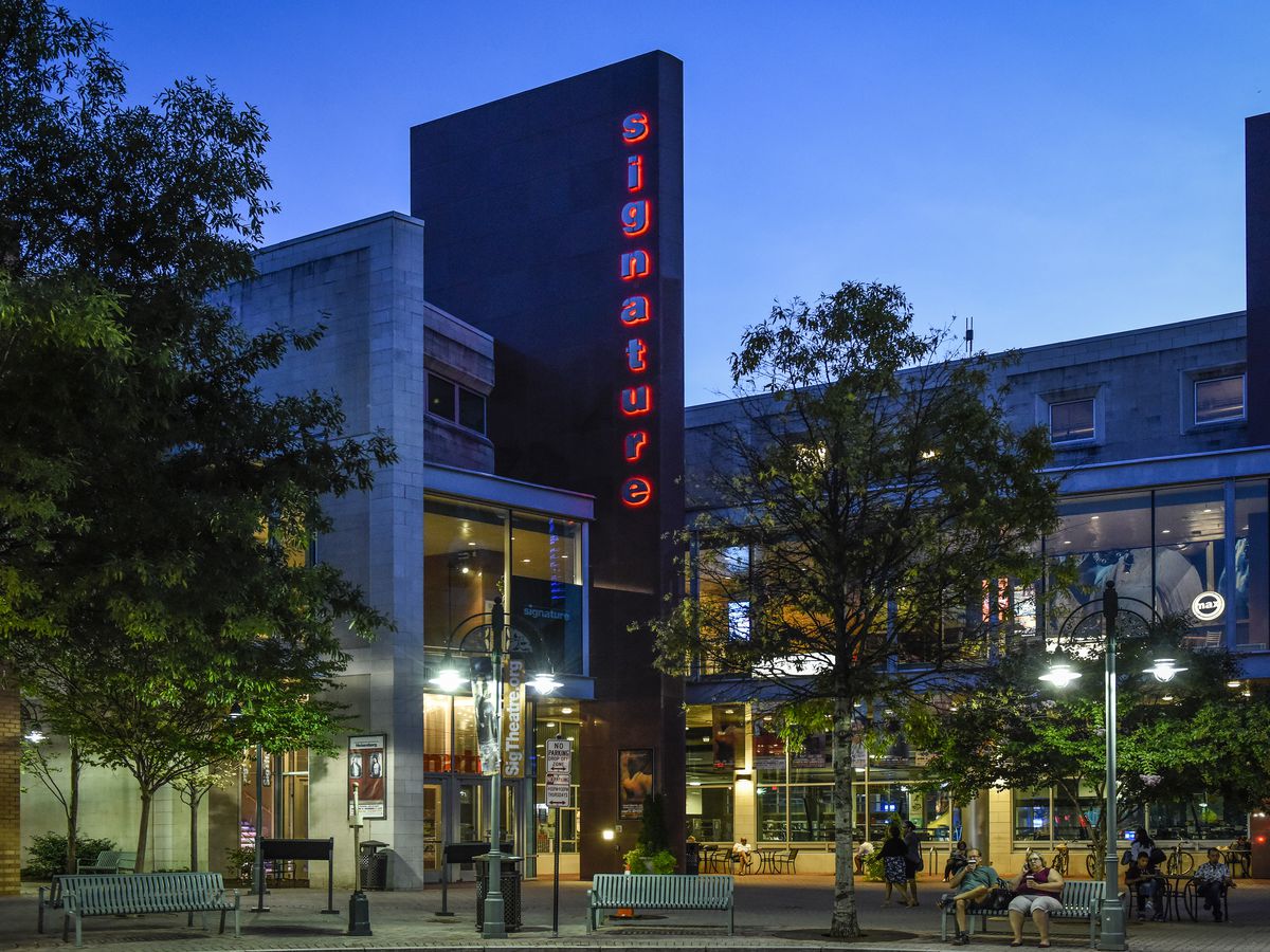 A modern theater building surrounded by trees and benches.