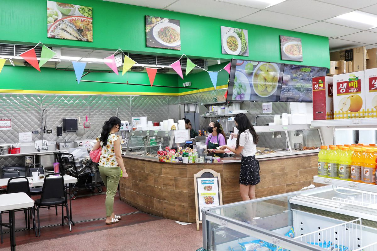Two women stand in front on an L-shaped counter while a woman behind serves them