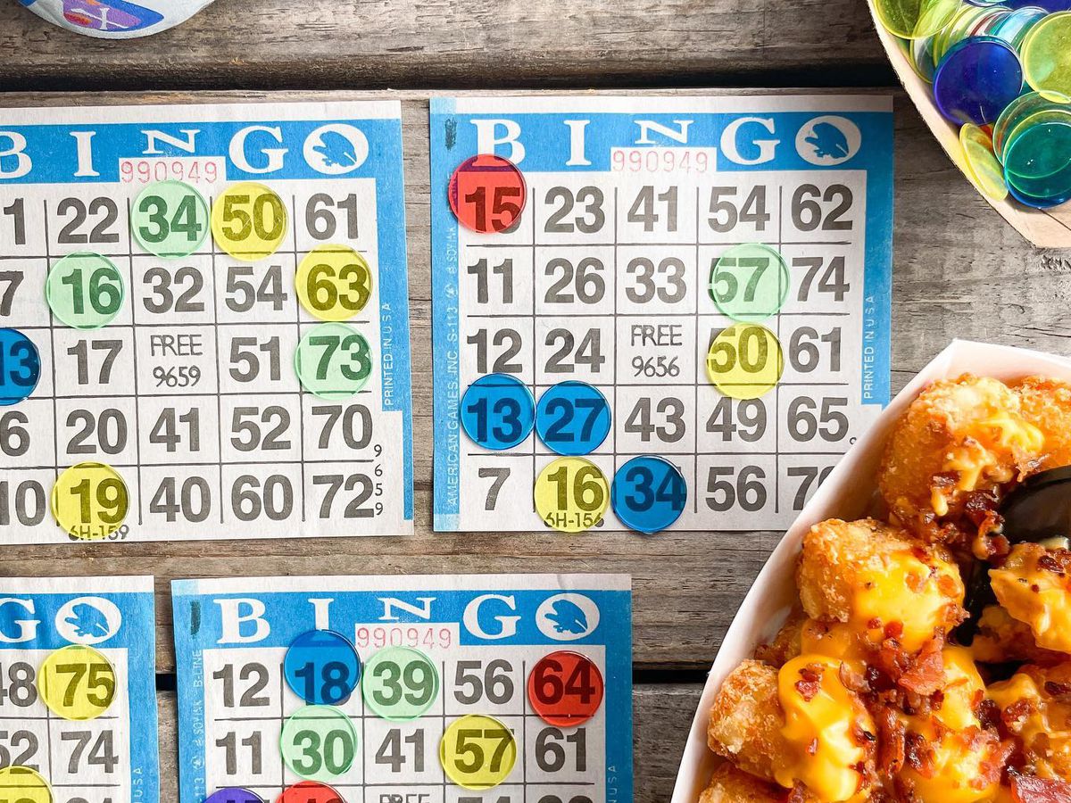 Four bingo cards with yellow, green, red, and blue chips sits beside a can of beer, a basket of bingo chips, and bacon and cheese covered tater tots at Red’s Beer Garden in Atlanta.