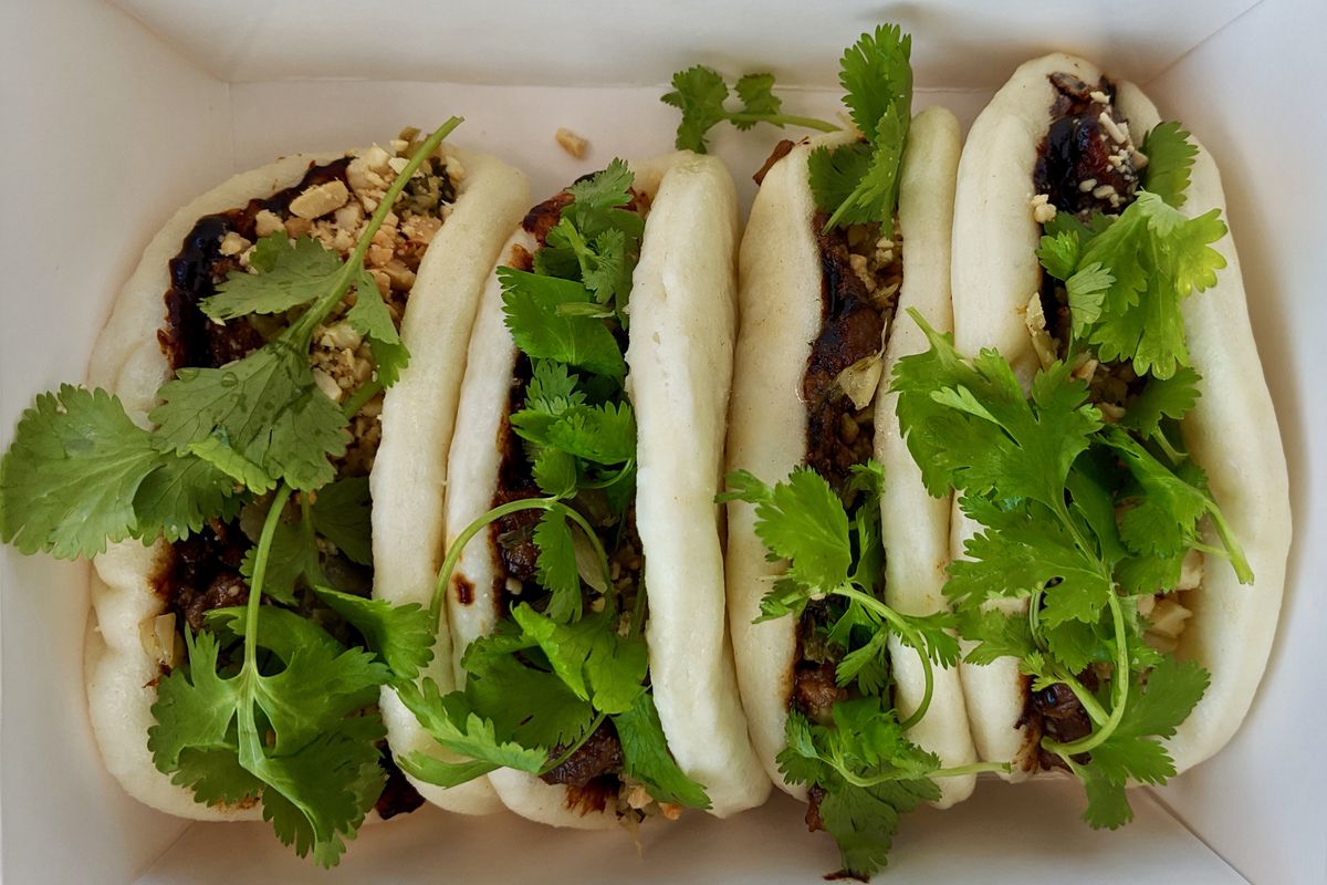 A takeout container comes with four buns dotted with crushed peanuts, cilantro, and meat at Chit-Chat Cafe