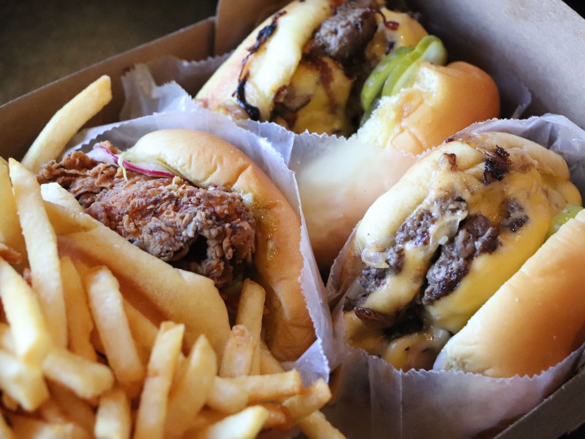A collection of burgers and a fried chicken sandwich, along with fries, in a cardboard box.