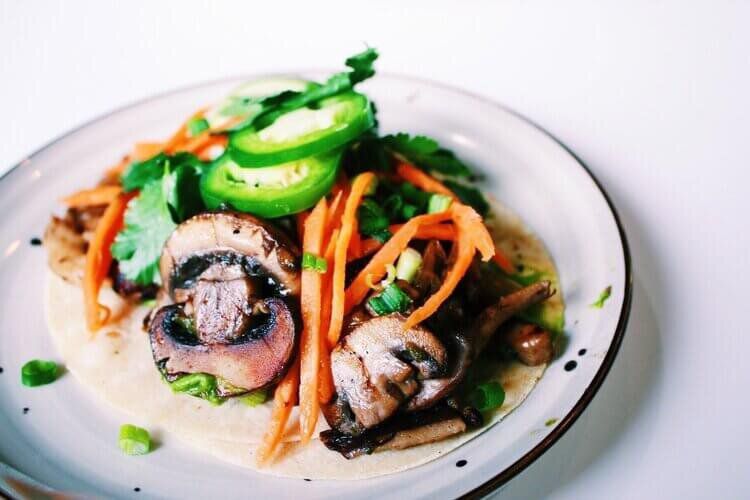 A brightly lit plate of mushroom tacos topped with shreds of carrots and coins of jalapeños