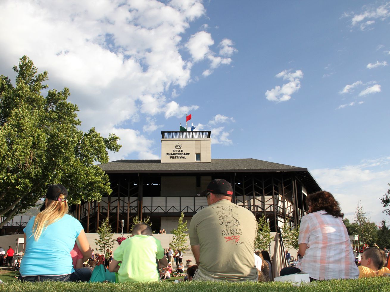 People lounging on the grass at the Greenshow at the 2017 Utah Shakespeare Festival, with the Engelstad Shakespeare Theatre in the background. On Monday, the festival announced its 2021 season. 