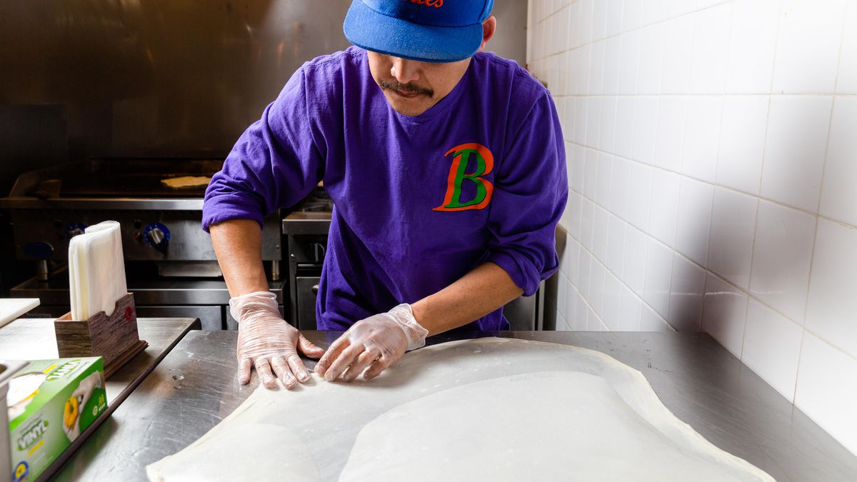 The owner of Burmese Bites stretching out dough to make palata on a steel tabletop.