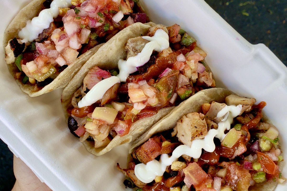 A takeout container filled with three chicken tacos topped with mayo, salsa, and pico de gallo