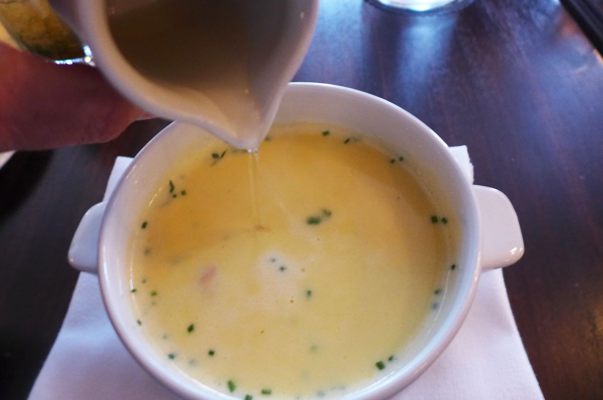 A bowl of yellow soup, with a small pitcher poised overhead.
