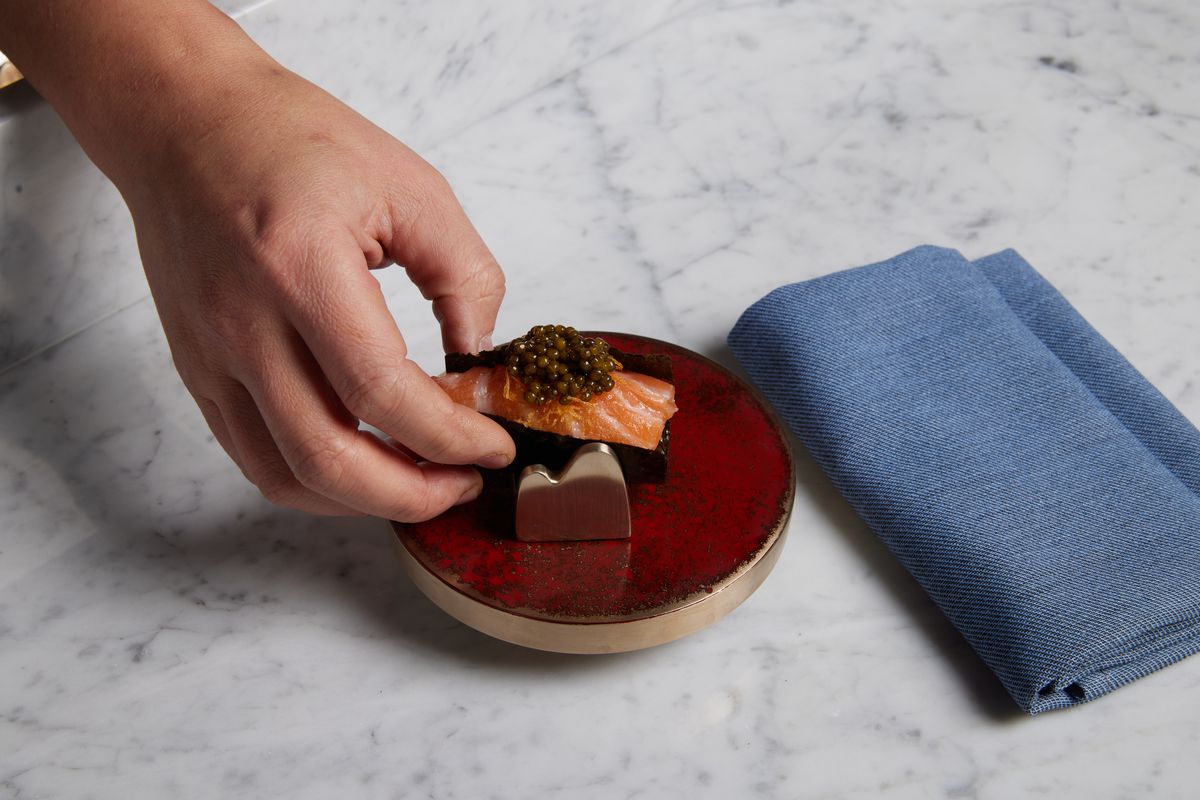 Caviar sits atop a slice of king salmon in a hand roll; a hand is visible picking up the roll