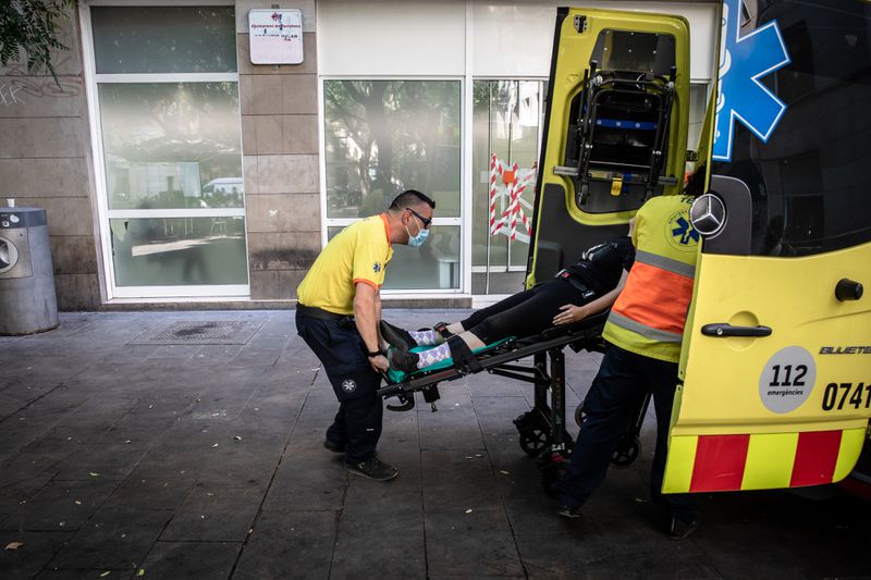 Paramedics wearing yellow shirts and black pants lift a patient on a stretcher into an ambulance.