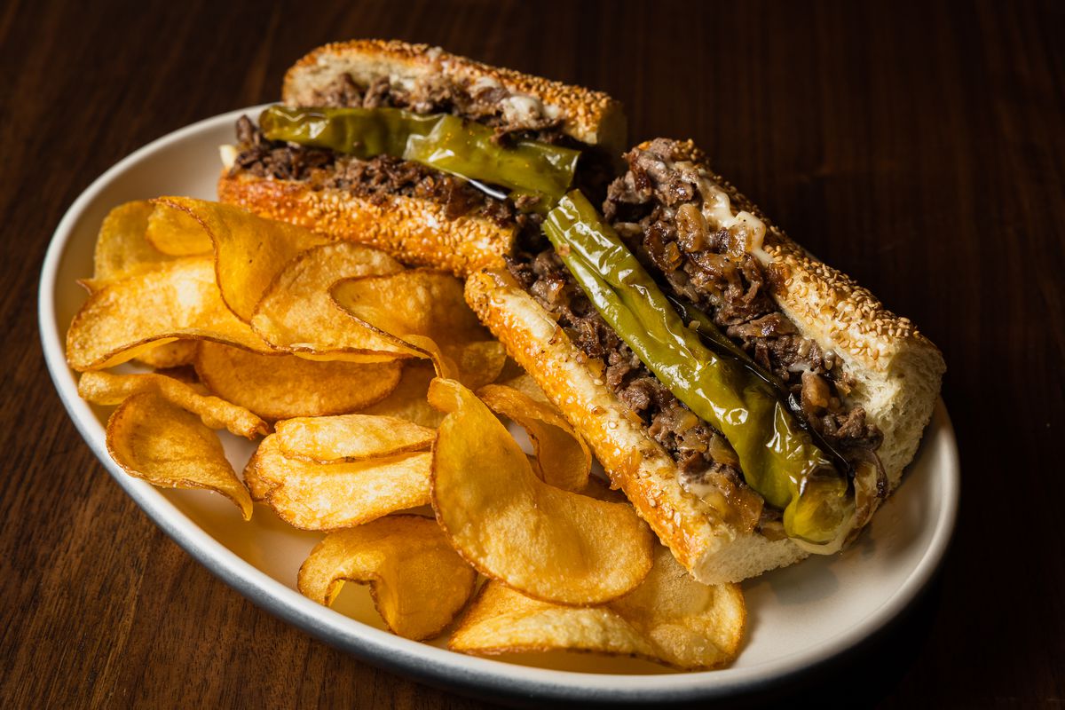 Wagyu cheesesteak with chips on a plate.